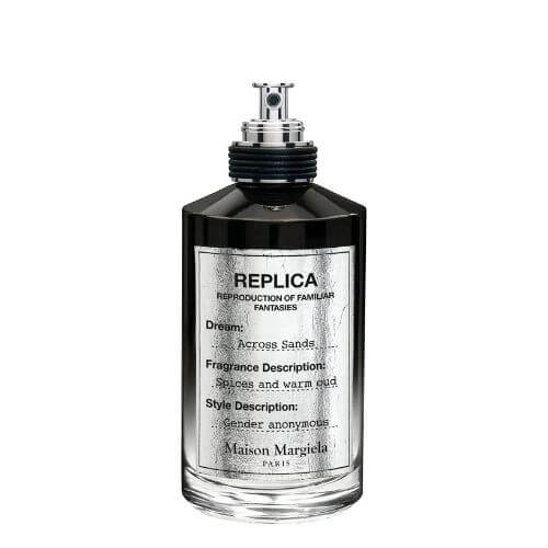 Clear fragrance bottle labeled Across Sands Eau de Parfum, 100 ml, simple white label and capped sprayer, resting amid golden-toned sand imagery.