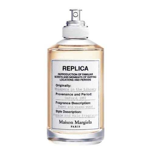 Clear glass perfume bottle labeled ‘Replica Whispers in the Library Eau de Toilette’ (100 ml), shown next to its matching box with a subtle, vintage-style library scene.